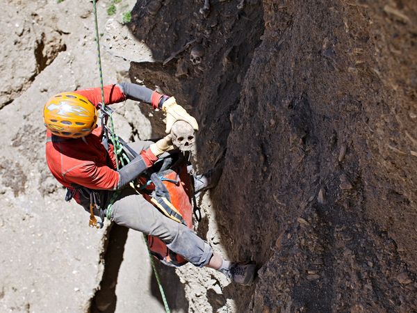 Pete Athans, esperto scalatore, recupera resti umani dalla parete rocciosa; sullo sfondo, un altro cranio umano (Cory Richards)