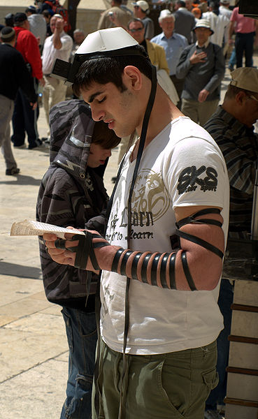 Un uomo davanti al Muro Occidentale che indossa i tefillin della testa e del braccio (wikimedia)